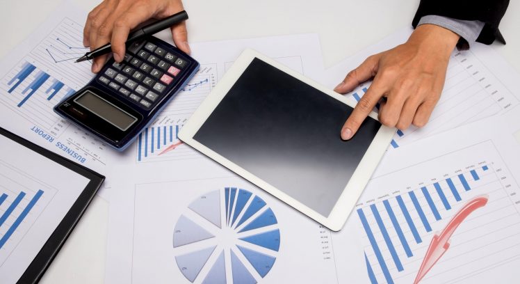 business documents on office table with smart phone and digital tablet and man working in the background.