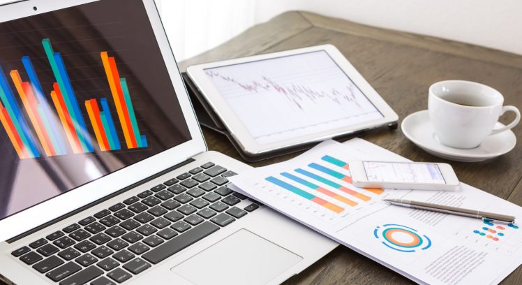 Laptop, tablet , smartphone and coffee cup with financial documents on wooden table