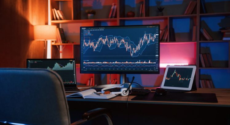 Computer with stock exchange graph on display is in the dark room with neon lighting.